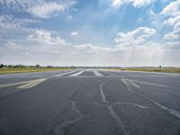 an empty runway surrounded by green grass and trees with a blue sky with fluffy clouds