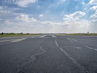 an empty runway surrounded by green grass and trees with a blue sky with fluffy clouds