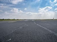 an empty runway surrounded by green grass and trees with a blue sky with fluffy clouds