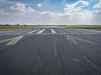 an empty runway surrounded by green grass and trees with a blue sky with fluffy clouds