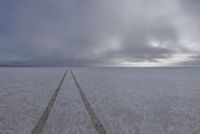 a lone road is in a vast open field, while thick snow surrounds the plains