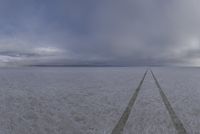 a lone road is in a vast open field, while thick snow surrounds the plains