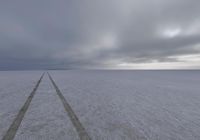 a lone road is in a vast open field, while thick snow surrounds the plains