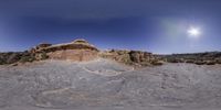 an arid area with rock formations and large rock carvings, with the moon in the blue sky above them