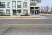 an empty street in front of a modern apartment building with balconies on the first floor