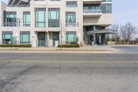 an empty street in front of a modern apartment building with balconies on the first floor