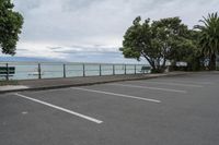 a parking lot is lined with trees next to the ocean and a bench sitting at the edge of it