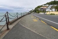 a road with a fence on it leading to a body of water and a beach