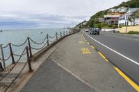 a road with a fence on it leading to a body of water and a beach