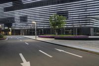 a street light on a road in front of a tall building at night with a sidewalk