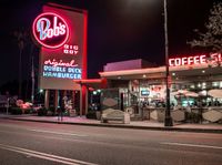 a coffee shop lit up at night on a city street with no one on it