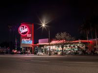 a red lit diner next to a palm tree lined street at night time with cars parked on side