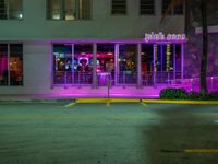 neon lights in the windows of an illuminated building in the night time on a sidewalk