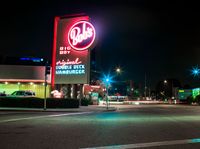 a city intersection filled with cars at night time next to a neon sign that says waffle