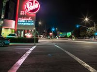 a city intersection filled with cars at night time next to a neon sign that says waffle