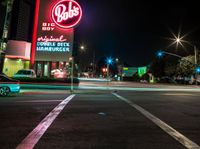 a city intersection filled with cars at night time next to a neon sign that says waffle