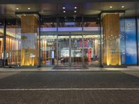 a man walking past an empty building with glass doors on it at night time with lights shining on