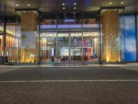 a man walking past an empty building with glass doors on it at night time with lights shining on