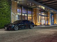 a very nice looking car parked by some nice architecture at night time with the lights on