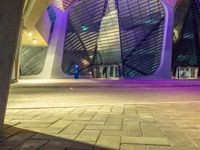 the walkway outside of a building at night with a traffic light in the foreground