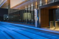 an empty city sidewalk near the windowed walkway at night with a blue light in the foreground