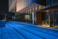 an empty city sidewalk near the windowed walkway at night with a blue light in the foreground