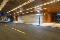 a empty empty street under an overpass at night, near a city building and lamp posts