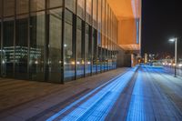 an illuminated walkway leading to a modern building at night with lights shining brightly on the pavement