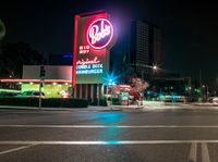 the neon sign for cola's big krob restaurant sits next to a street