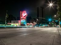 a very tall neon sign over a busy street at night time and a couple cars driving in the distance