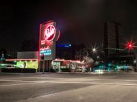 a very tall neon sign over a busy street at night time and a couple cars driving in the distance