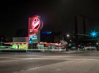 a very tall neon sign over a busy street at night time and a couple cars driving in the distance