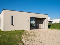 the building is standing on the sand with its door open and grass in front of it