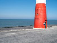 a person on a bicycle is riding next to a lighthouse on the road by the water