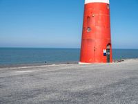 a person on a bicycle is riding next to a lighthouse on the road by the water