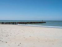 the view of an empty beach with wooden structure in the water in the distance,