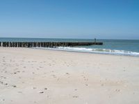 the view of an empty beach with wooden structure in the water in the distance,