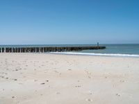 the view of an empty beach with wooden structure in the water in the distance,