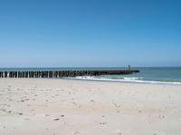 the view of an empty beach with wooden structure in the water in the distance,