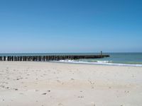 the view of an empty beach with wooden structure in the water in the distance,