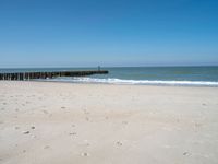 the view of an empty beach with wooden structure in the water in the distance,