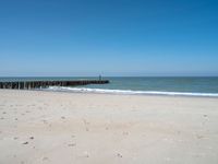 the view of an empty beach with wooden structure in the water in the distance,