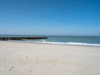 the view of an empty beach with wooden structure in the water in the distance,