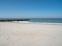 the view of an empty beach with wooden structure in the water in the distance,