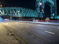 a big bridge across a road in the night time with lights coming down and buildings in the distance