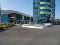 a large, curved building is seen with a pedestrian foot bridge going through it and bushes on either side