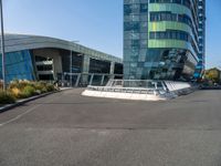 a large, curved building is seen with a pedestrian foot bridge going through it and bushes on either side