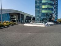 a large, curved building is seen with a pedestrian foot bridge going through it and bushes on either side