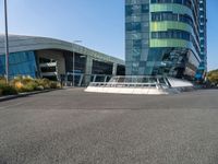 a large, curved building is seen with a pedestrian foot bridge going through it and bushes on either side