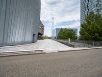 an outdoor area with some stairs, cars and buildings in the background, under a cloudy blue sky